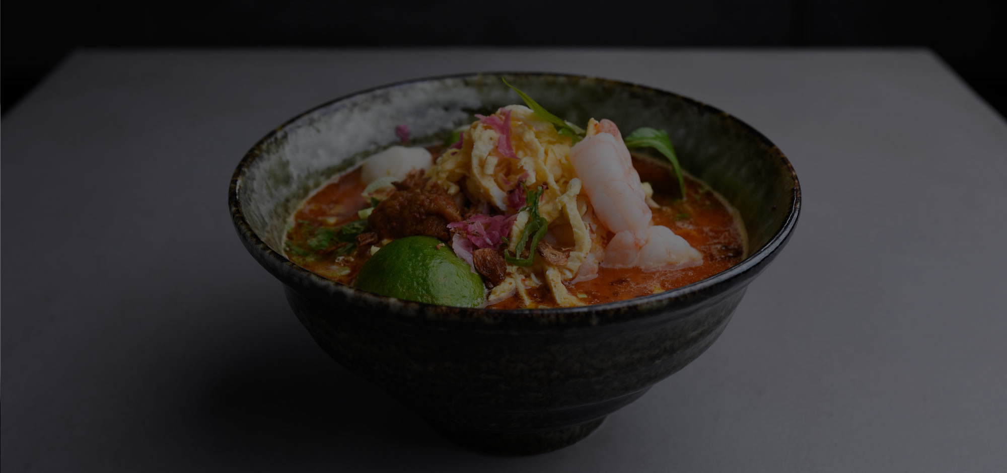 A bowl of Laksamania curry laksa with king prawns, shredded egg and lime