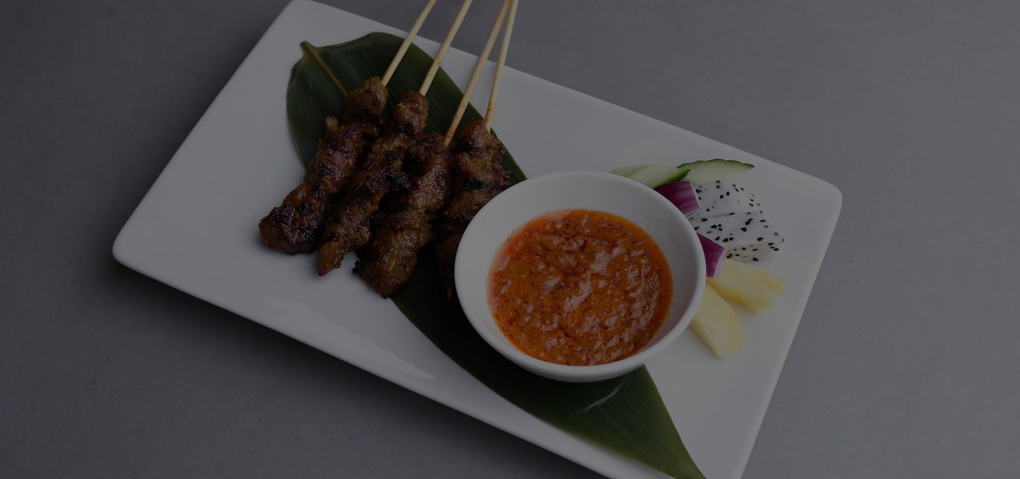 Charcoal-grilled Malaysian satay skewers with peanut dipping sauce and fresh fruit